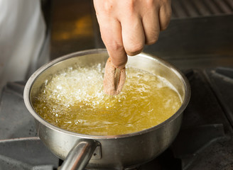 Calamari ring being placed into a pan of hot bubbling oil.