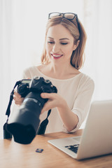 Vertical portrait of young pretty photographer looking at camera in her hands and sitting at the...