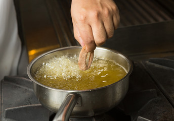 Calamari ring being placed into a pan of hot bubbling oil.