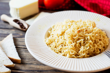 Hearty and delicious dinner, pasta, instant noodles with spices, tomatoes and mozzarella cheese on a dark wooden background 