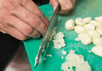 Finely chopped garlic on a green cutting board, sliced by a knife.
