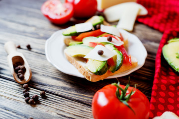 Healthy, wholesome and healthy breakfast or lunch, sandwiches with fresh avocado with spices, mozzarella cheese and tomato on a dark rustic wooden background