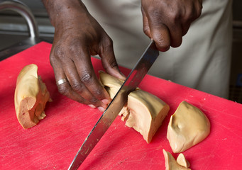 a knife slicing through fresh Foie Gras, on a red cutting board.