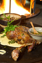 Delicious free range roasted goat shoulder served on a rustic metal plate by a hot open coal fire. Served with fresh parsley.