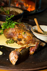 Delicious free range roasted goat shoulder served on a rustic metal plate by a hot open coal fire. Served with fresh parsley.