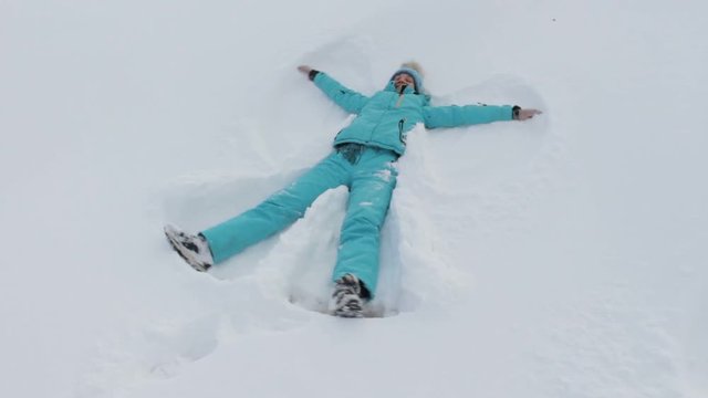 Young woman in blue ski clothes making snow angel