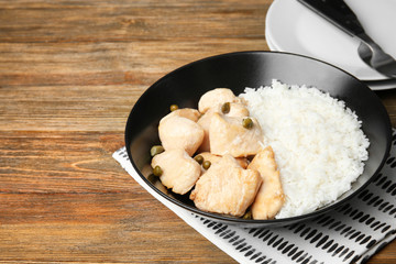 Black plate with delicious chicken and rice on wooden table
