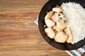Black plate with delicious chicken and rice on wooden table