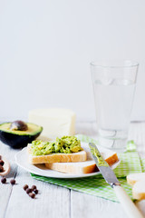 Healthy, wholesome and healthy breakfast or lunch, sandwiches with puree from fresh avocado with spices, mozzarella cheese and mineral water on a light rustic wooden background 