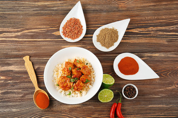 Plate with tasty chicken tikka masala, rice and spices on wooden table
