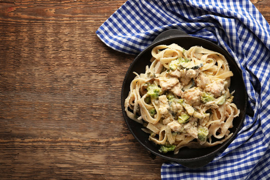 Frying pan with delicious chicken Alfredo on wooden table