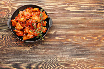 Frying pan with delicious chicken tikka masala on wooden table