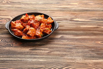 Frying pan with delicious chicken tikka masala on wooden table