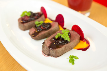 Organic Venison served with fresh raspberry raspberry sauce, beetroot slices and pumpkin puree, on a white plate.