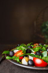 Classic Italian salad with mozzarella, tomatoes, basil, olives and olive oil. Caprese in a clay bowl on a wooden background. Copy space.