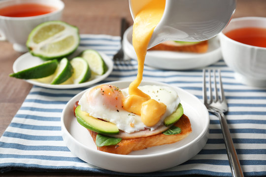Pouring hollandaise sauce onto egg Benedict on plate