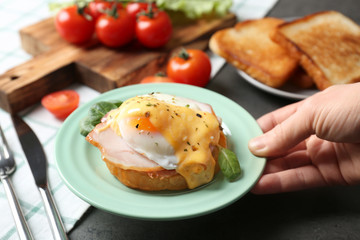 Female hand putting plate with tasty egg Benedict on table