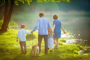 complete family consisting of a father, mother, son, daughter and their dog Beagle, walk in the evening haze at the lake