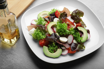 Plate with fresh salad and bottle of oil on table