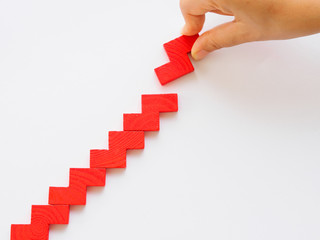 Concept of building success foundation. Women hand put red puzzle wooden blocks in the shape of a staircase