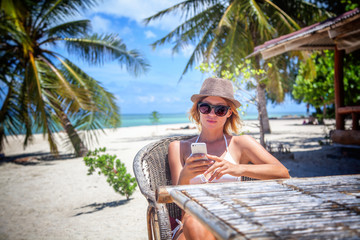 Young beautiful woman with mobile phone on the shore of the tropical sea in a cafe. Communication...