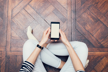 Girl in jeans sitting on the floor at home and using a mobile phone