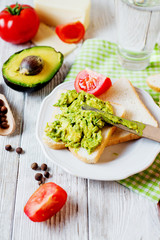 Healthy, wholesome and healthy breakfast or lunch, sandwiches with mashed potatoes from fresh avocado with spices, mozzarella cheese, tomato and mineral water on a light wooden background 
