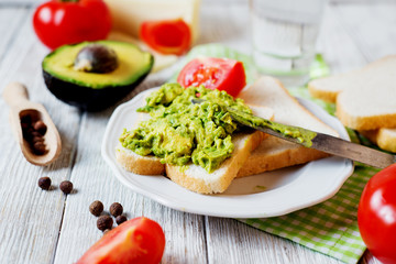 Healthy, wholesome and healthy breakfast or lunch, sandwiches with mashed potatoes from fresh avocado with spices, mozzarella cheese, tomato and mineral water on a light wooden background 