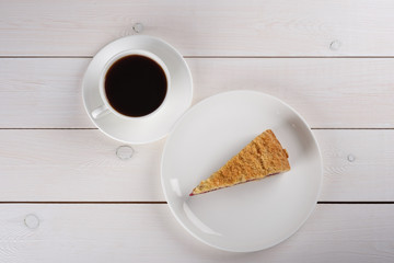 A cup of black coffee and a piece of berry pie on a plate stand on a white wooden table. Top view
