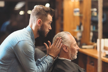Stylish barber shaping haircut of the client in the barbershop