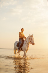 Macho man and horse on the background of sky and water. Boy model, cowboy on horseback on the beach...