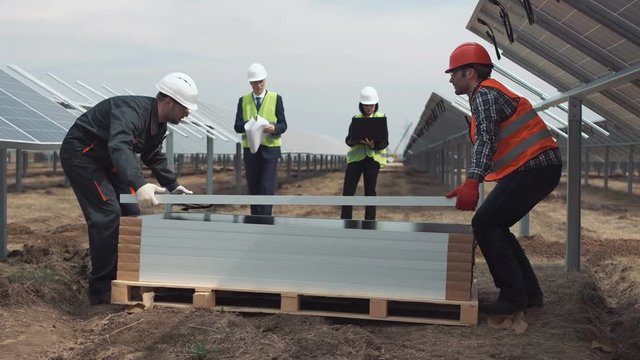 The supervisors with plan looking at builders mounting the solar energy panels. They holding notebook laptop and blueprints.