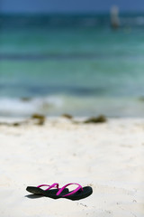 Naklejka premium Sandals on the beach. White sand. Turquoise water. Focus point on the flip-flops.