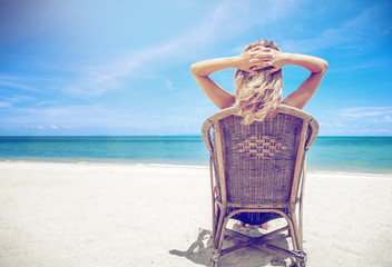 Fototapeta na wymiar A blond woman in a hat sits on a chair and looks at a beautiful seascape, the Maldives Islands, a tropical paradise