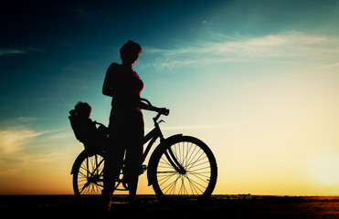 Obraz na płótnie Canvas Silhouette of mother and baby biking at sunset