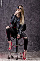 Obraz na płótnie Canvas Beautiful urban trendy girl in black leather jacket and jeans posing on a high chair