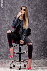 Fototapeta na wymiar Beautiful urban trendy girl in black leather jacket and jeans posing on a high chair