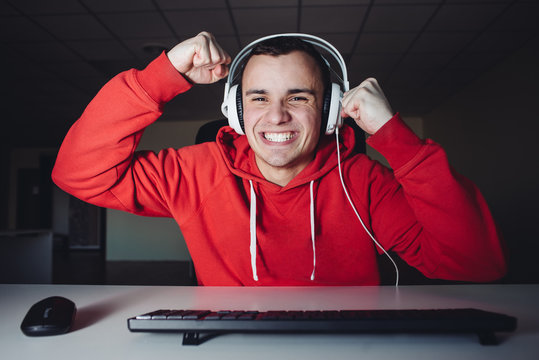 Joyful young man with headphones at home playing a computer game. Gamer happy for the win.