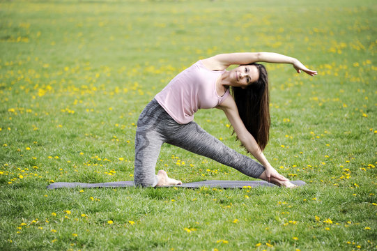 Beautiful young woman is doing yoga in the park. Gate pose. Healthy lifestyle concept.