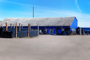 landscape of blue warehouse and pvc black plastic pipe stacks for plumbing in front the building