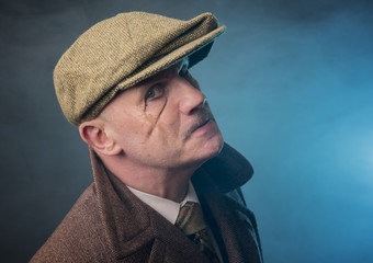 Mature man dressed as an English 1920s gangster, on a blue smoky background