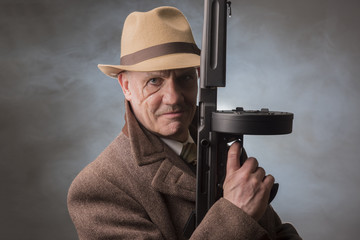  1940s male gangster holding a machine gun, on a grey smoky background 