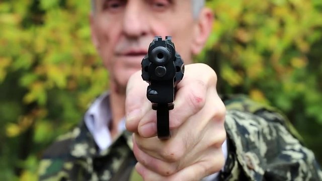 Man holds in hand black revolver and looks at the camera. Retired officer in military uniform at shooting range