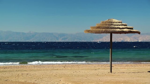 Red sea, gulf of Aqaba, umbrella on the beautiful beach. Tropical resort in Tala Bay, Hashemite Kingdom of Jordan. View on Israel and Egypt on the other coast
