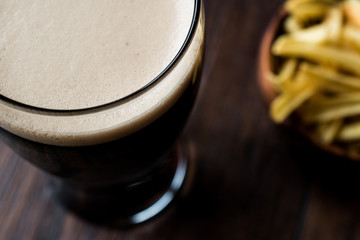 Dark Beer with snacks potato chips on wooden surface.
