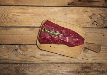 Raw beef steak on a cutting board with rosemary and spices.