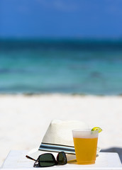 Cold beer on the beach. White table along with sunglasses and a summer hat. Relaxing vacation concept image. 