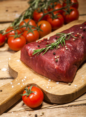Raw beef steak on a cutting board with rosemary and spices.