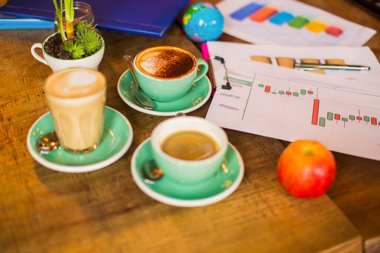 Photo of a table with cups of coffee, with apple, with papers, with folders, with globe, indoors