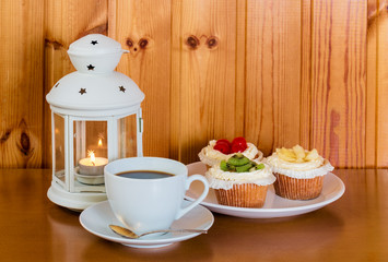Cup of coffee, sweet cakes with fruits and lantern on wooden table